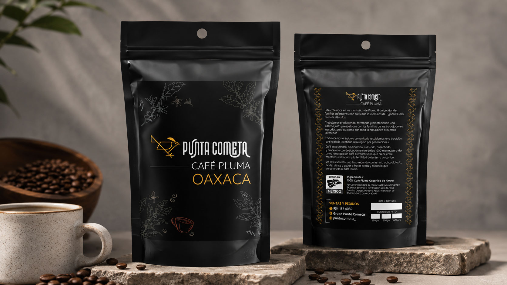 Frente y reverso de dos bolsas negras de café Punta Cometa Café Pluma Oaxaca sobre una piedra, junto a una taza y granos de café
