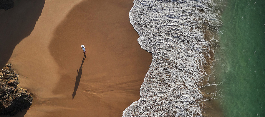 Vista aérea de una persona caminando por una playa de arena junto a las olas del Pacífico