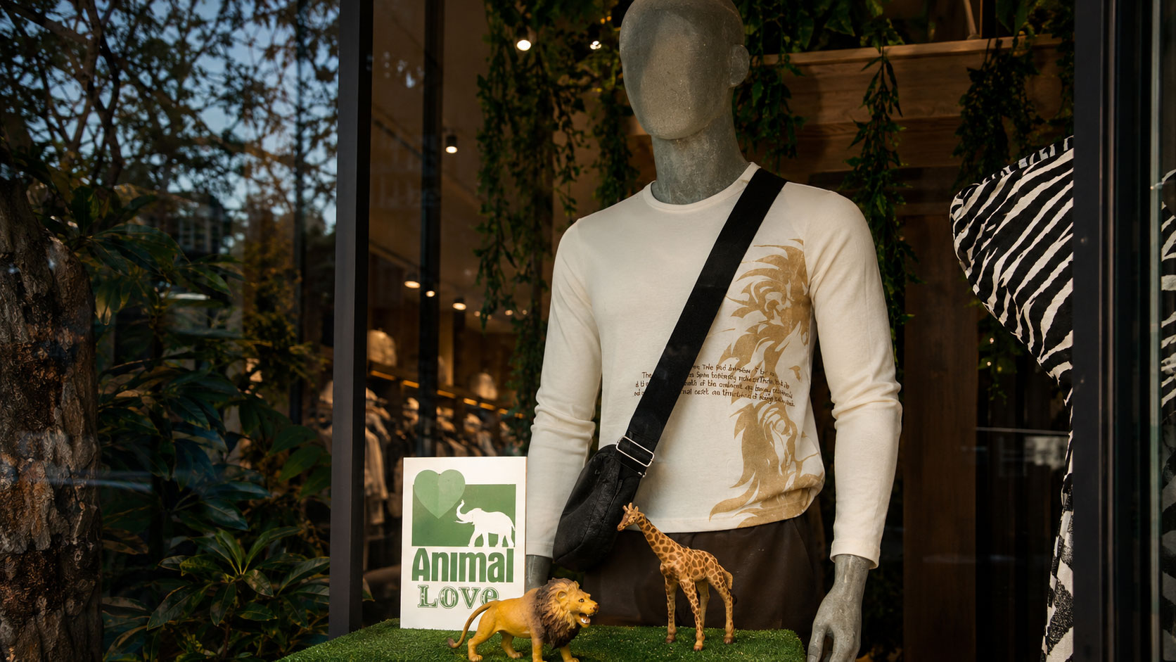 Escaparate con un maniquí que viste un suéter crema con un gráfico dorado de un león, junto a figuras de un león y una jirafa y un letrero de Animal Love