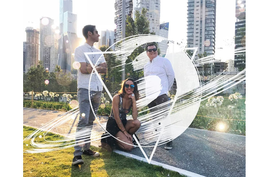 Tres integrantes de la banda SaturnoV posando al aire libre frente a rascacielos, con el logo de la banda sobre la fotografía