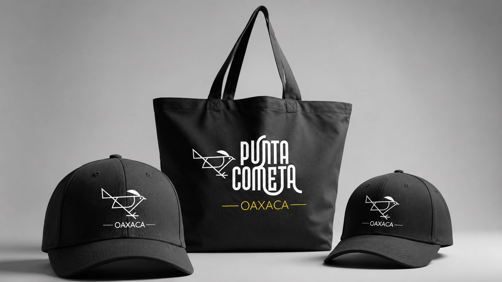Gorras negras y una bolsa tote con el logotipo de Punta Cometa Oaxaca sobre fondo gris